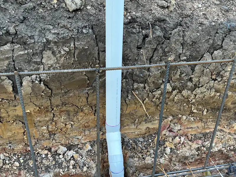 New PVC drainage riser standing in an excavated trench beside steel reinforcing for a new slab
