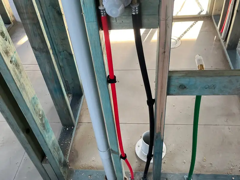 Shower mixer rough-in with red and black water pipes and a floor waste inside a timber wall frame