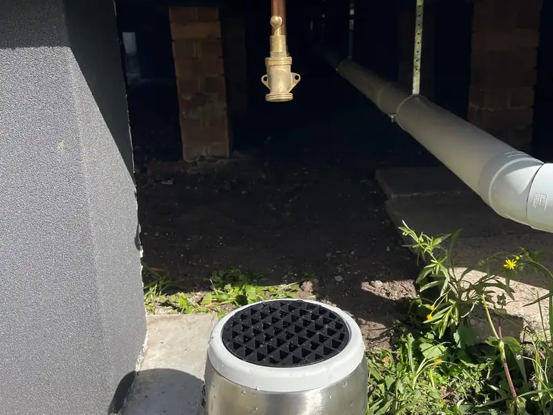 New brass hose tap under a raised floor beside an overflow relief gully with a steel collar