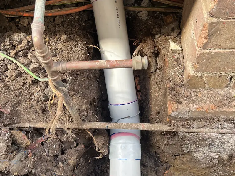 New grey PVC sewer pipe laid in an open trench beside a brick pier