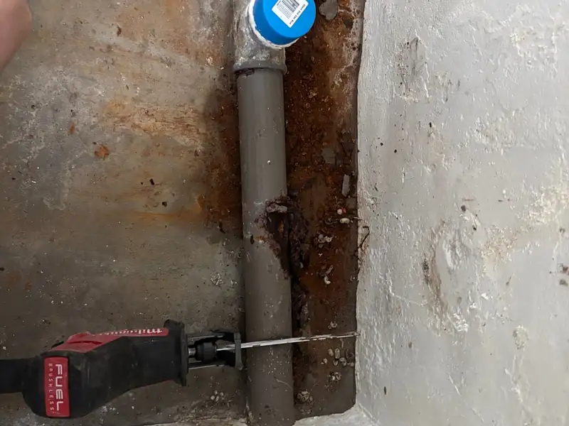 Grey pipe with a blue end cap beside a reciprocating saw during a pipe repair