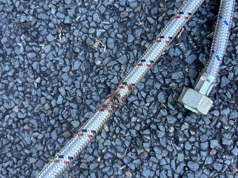 Removed braided flexible water hose with a burst section lying on gravel