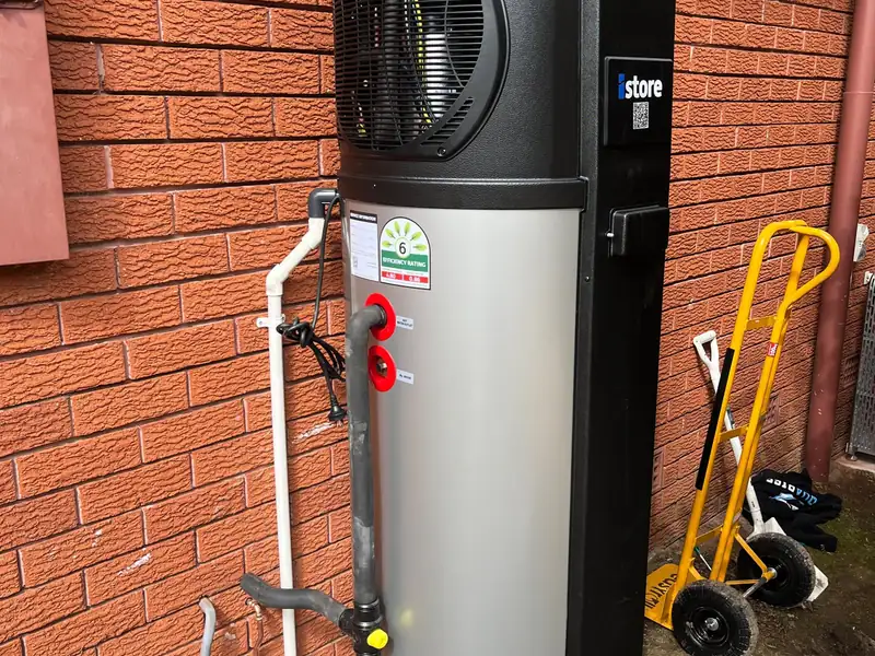 Heat pump hot water unit installed on a new concrete slab against a red brick wall