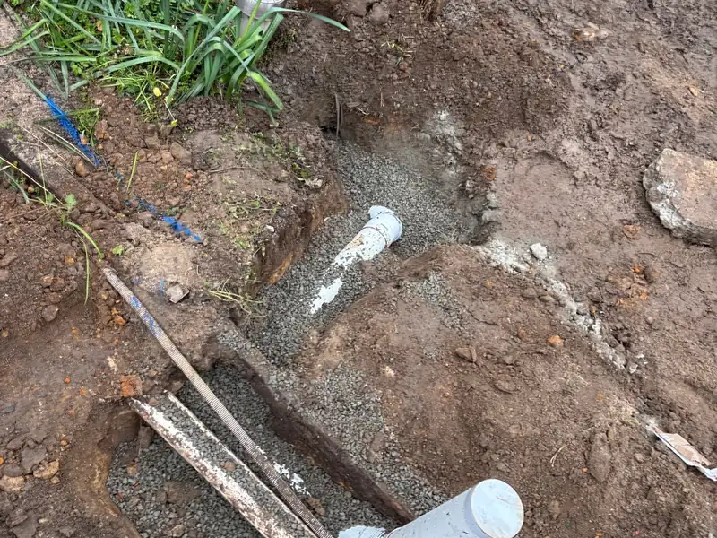 New PVC stormwater pipes with a capped end bedded in gravel in a trench beside a garden bed