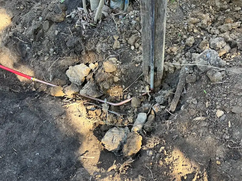 New copper water pipe laid through garden soil to the base of an outdoor tap on a timber post