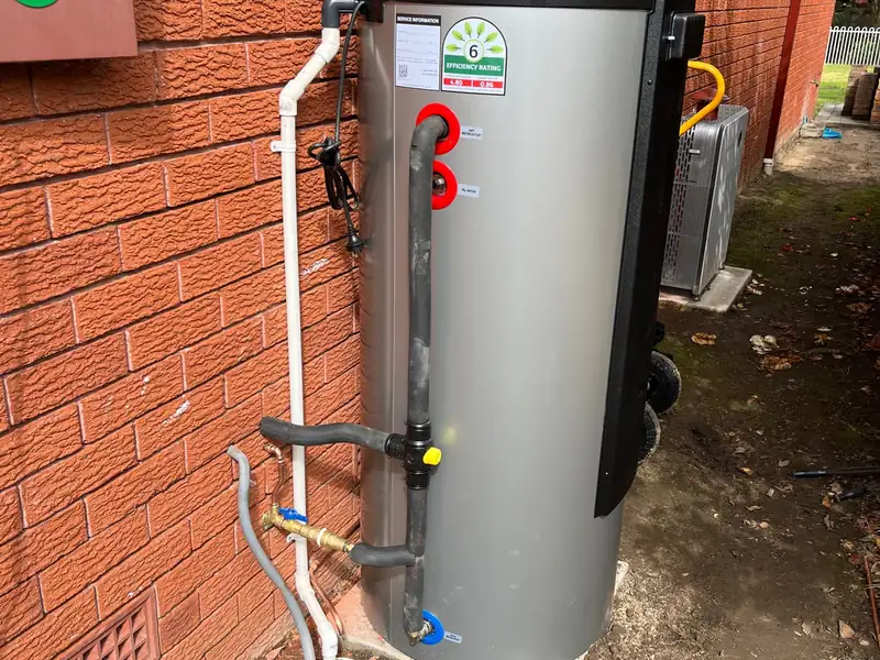 Newly installed heat pump hot water unit on a concrete slab beside a red brick wall