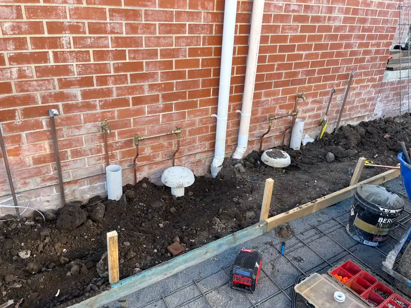 New brick wall on a building site with new copper pipework, taps, downpipes and formwork