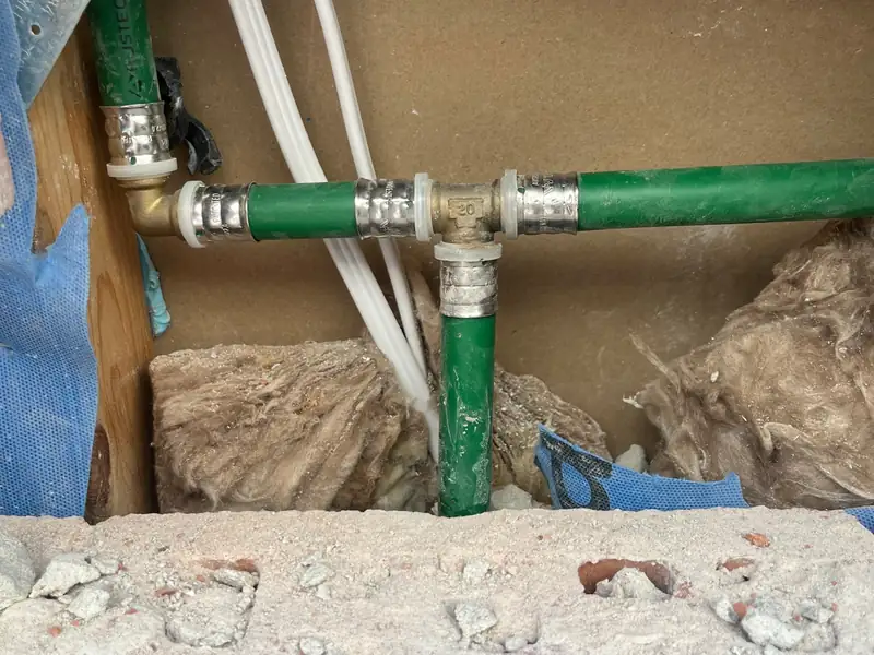 Close-up of a green water pipe tee with press fittings inside an opened wall cavity