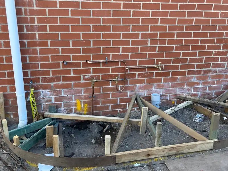 Copper water pipes, valves and a garden tap on the brick wall of a new home above slab formwork