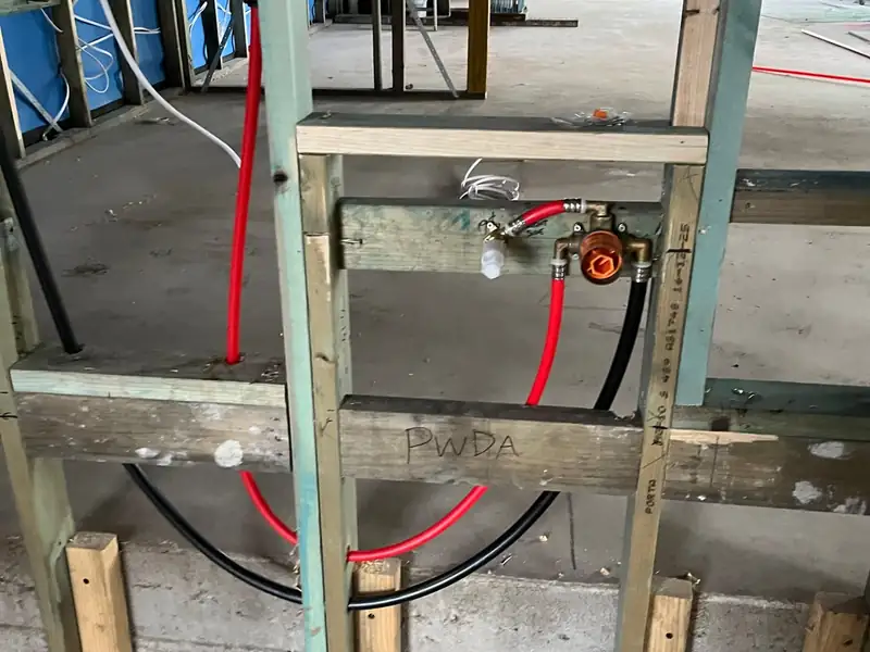 Red and black water pipes roughed in to a mixer on a timber noggin in a new house frame