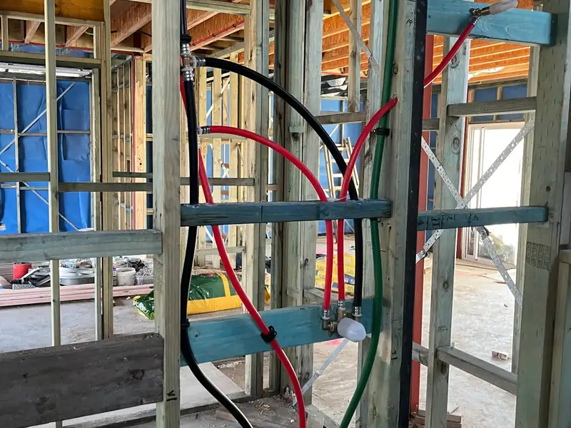 Red, black and green water pipes roughed in through the timber wall frames of a house under construction