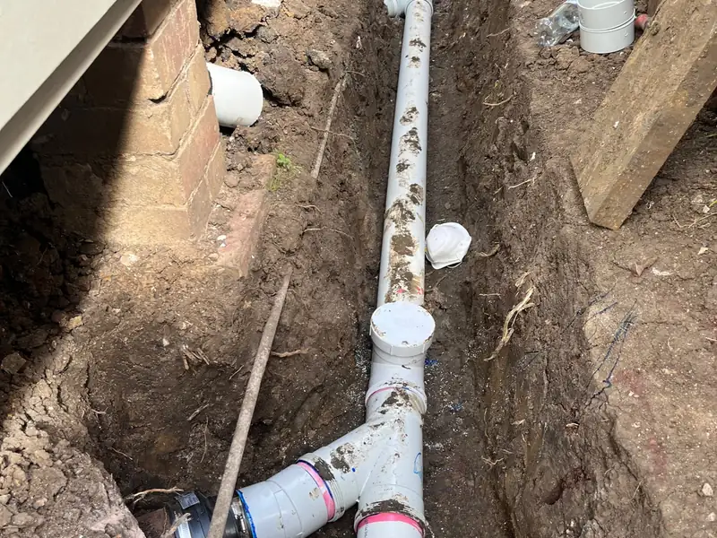 Long run of new PVC sewer pipe laid in a trench along the side of a house beside brick piers