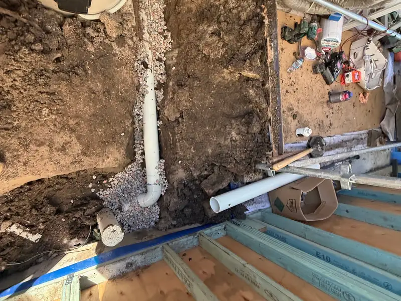 New white PVC sewer pipe bedded in gravel in a trench under a raised timber floor