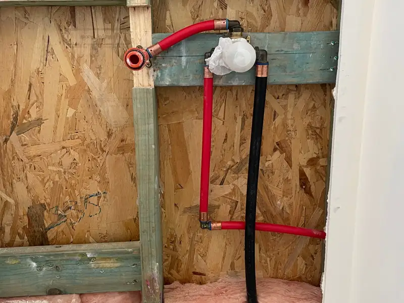 Opened wall cavity showing red and black water pipes connected to a mixer valve body