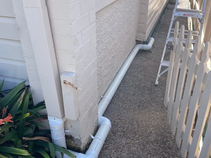 New white PVC stormwater line running along a side path from a downpipe, ladder beside it