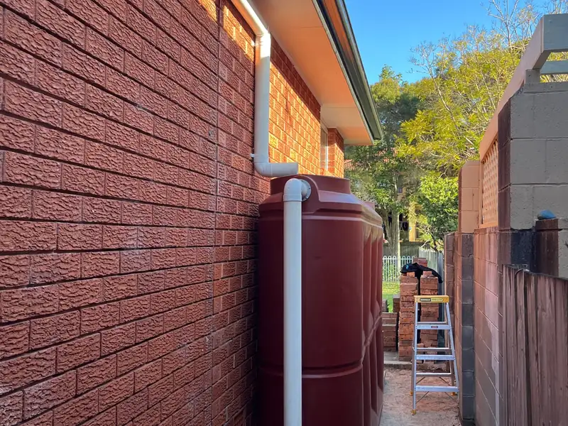 New white downpipe connected into a red rainwater tank, with a ladder standing beside it