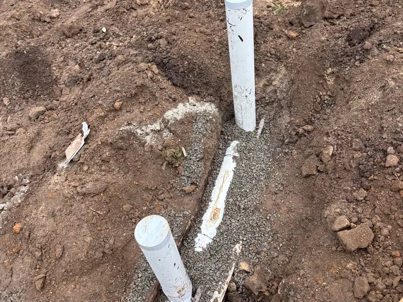 Two capped PVC risers and a new pipe bedded in gravel in an open stormwater trench
