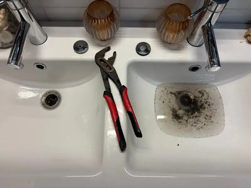 Double basin holding murky standing water before a blocked drain was cleared, pliers on the edge