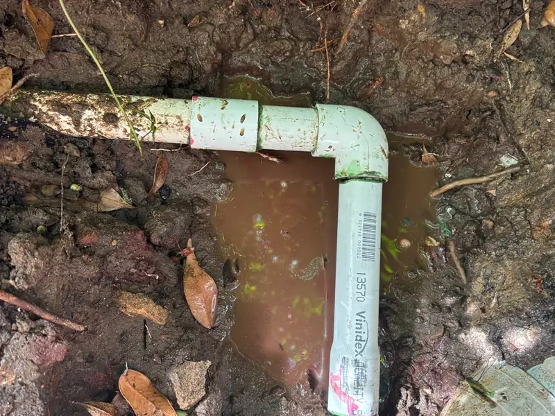 Repaired PVC pipe joint and elbow in a muddy excavated hole after a burst pipe repair