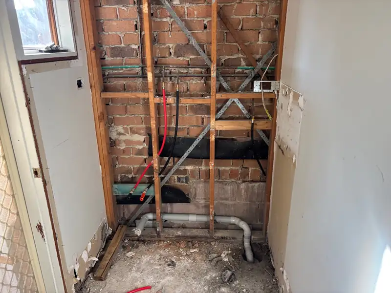 Stripped brick wall with new red and black water pipes and grey waste pipe roughed in