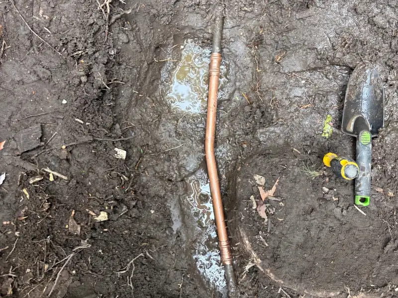 New copper pipe section joined into an existing line in a muddy excavated hole, trowel beside it