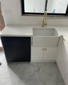 New laundry with a white farmhouse sink, brass tap and white cabinetry