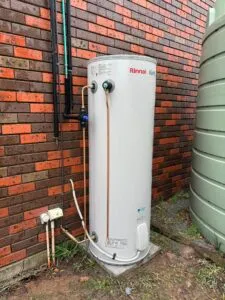 Electric hot water storage tank installed against a brick wall