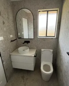 Renovated powder room with a vessel basin, black tapware, arched mirror and wall-faced toilet